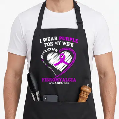 Fibromyalgia wife apron - I WEAR PURPLE FOR MY WIFE text around white heart with purple ribbon — shown on a black cotton canvas apron against a white background
