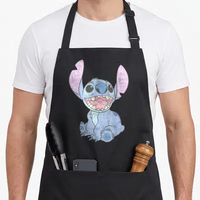 Portrait stitch apron - Blue cartoon creature with pink ears and wide open mouth sitting down — shown on a black cotton canvas apron against a white background