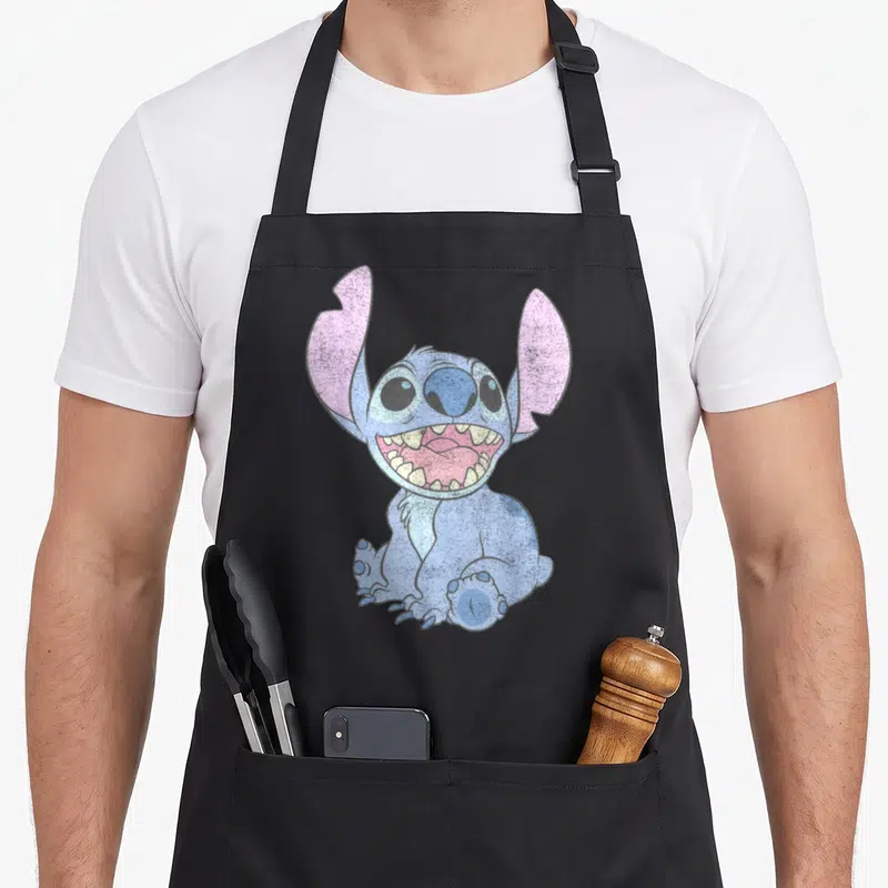 Portrait stitch apron - Blue cartoon creature with pink ears and wide open mouth sitting down — shown on a black cotton canvas apron against a white background
