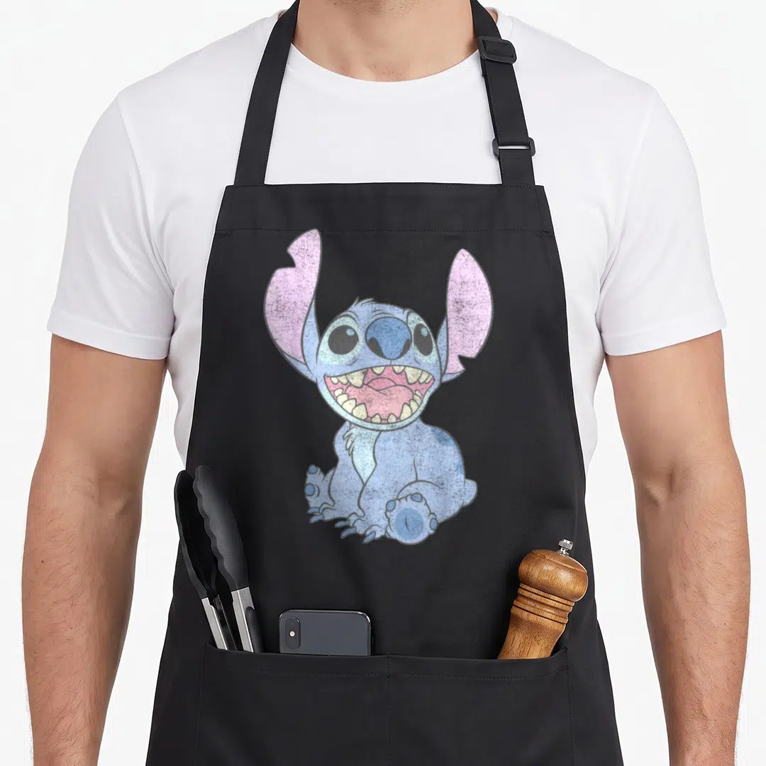 Portrait stitch apron - Blue cartoon creature with pink ears and wide open mouth sitting down — shown on a black cotton canvas apron against a white background