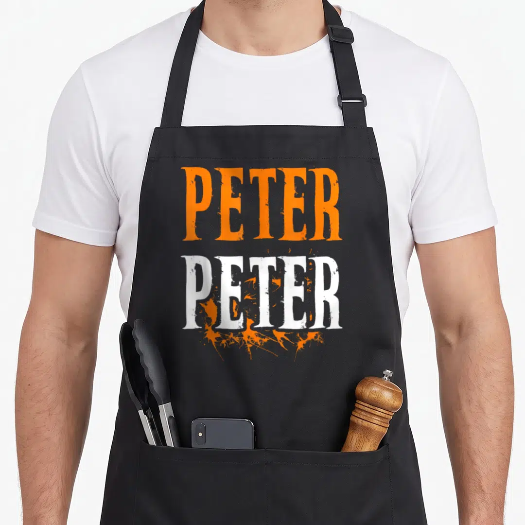 Splash halloween apron - Stacked PETER PETER text in orange and white with paint splatters — shown on a black cotton canvas apron against a white background