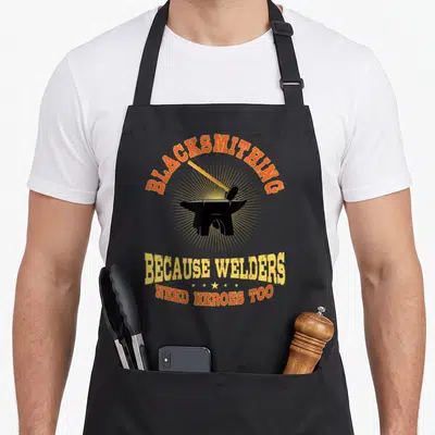 Metalworker blacksmith apron - Retro anvil and hammer graphic with orange and yellow text reading Because Welders Need — shown on a black cotton canvas apron against a white background