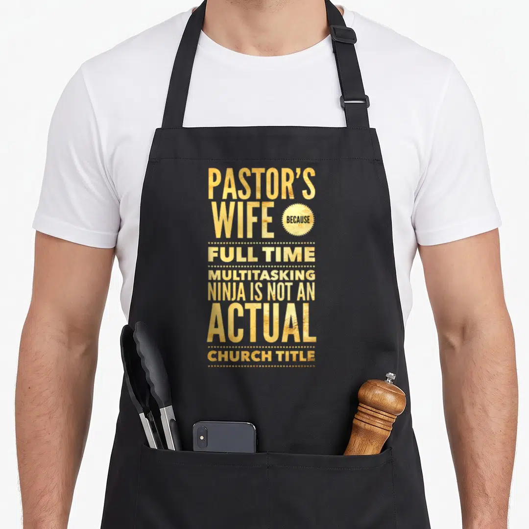 Pastoral wife apron - Gold stacked text reading Pastor's Wife Because Full Time Multitasking Ninja on black background — shown on a black cotton canvas apron against a white background