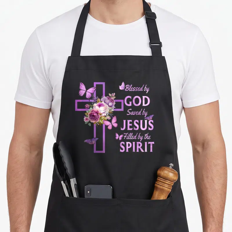 Blessed floral apron - Purple cross with pink flowers, butterflies, and text Blessed by God Saved by Jesus Filled — shown on a black cotton canvas apron against a white background
