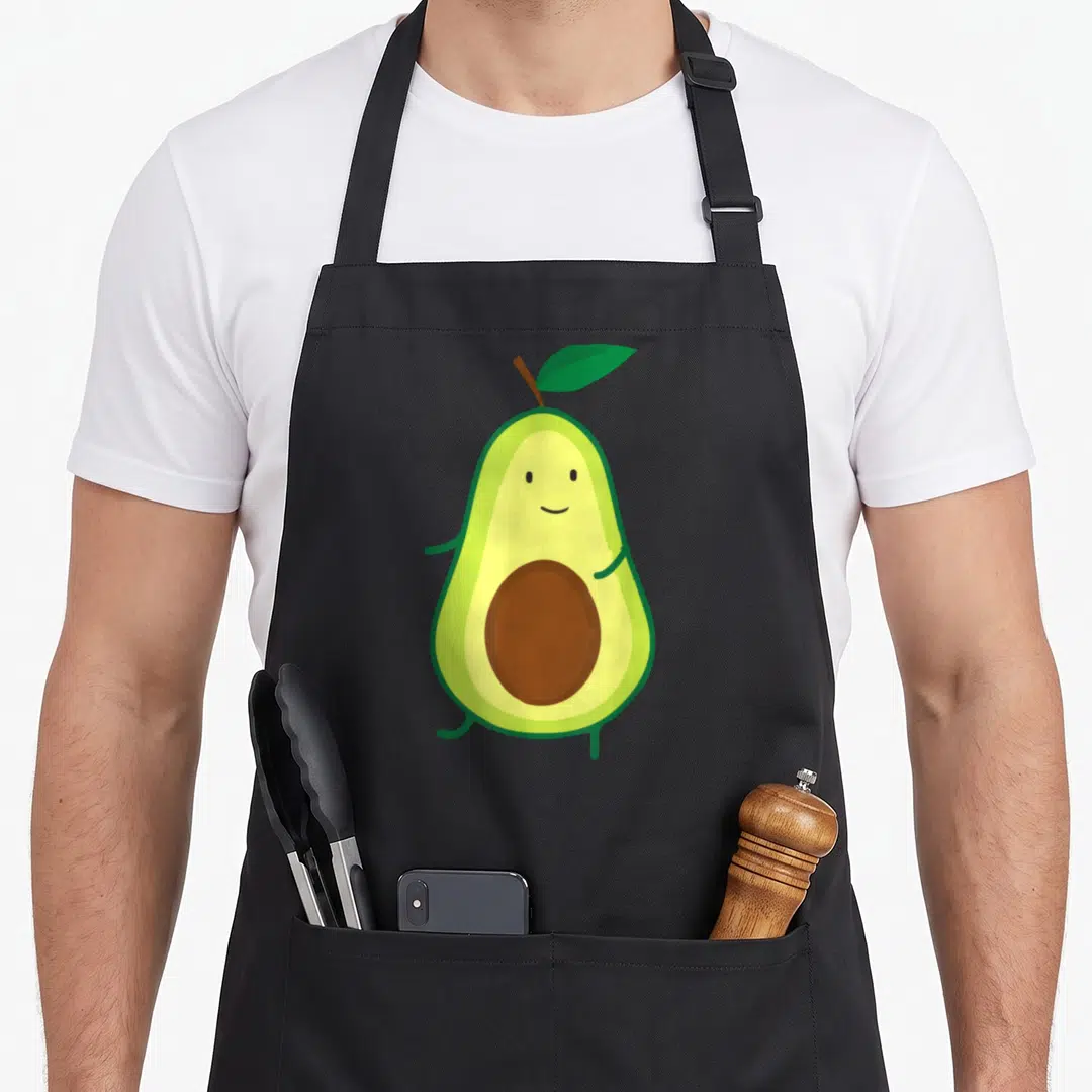 Mexican avocado apron - Smiling cartoon avocado with brown pit and green leaf — shown on a black cotton canvas apron against a white background