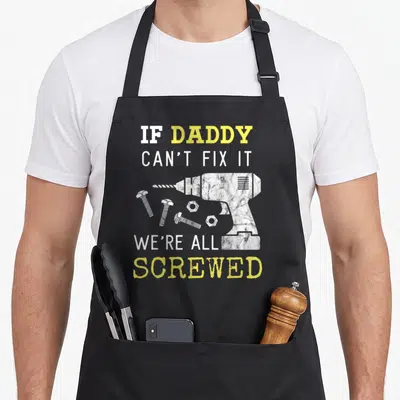 Wife handyman apron - Distressed drill and scattered screws with IF DADDY CAN'T FIX IT WE'RE ALL SCREWED text — shown on a black cotton canvas apron against a white background
