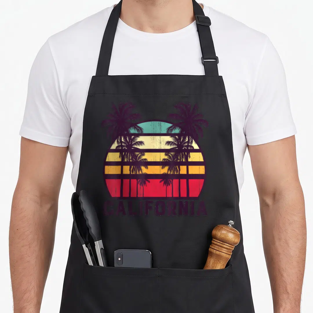 Skyline 70s apron - Retro California sunset with palm trees and colored horizontal stripes — shown on a black cotton canvas apron against a white background