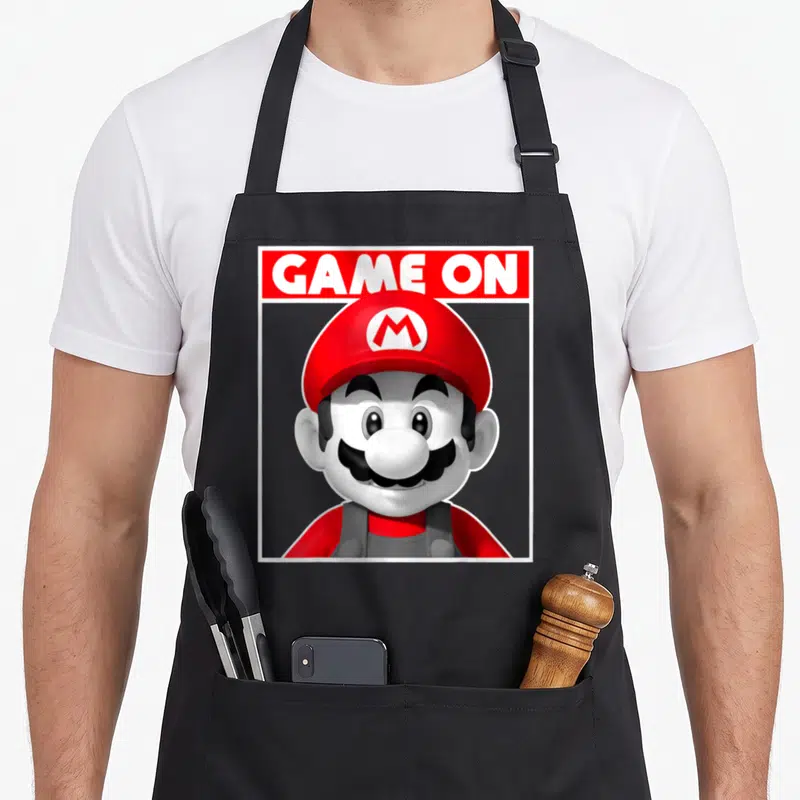 Box game aprons - Mario head and shoulders below GAME ON text in red rectangle with white border — shown on a black cotton canvas apron against a white background
