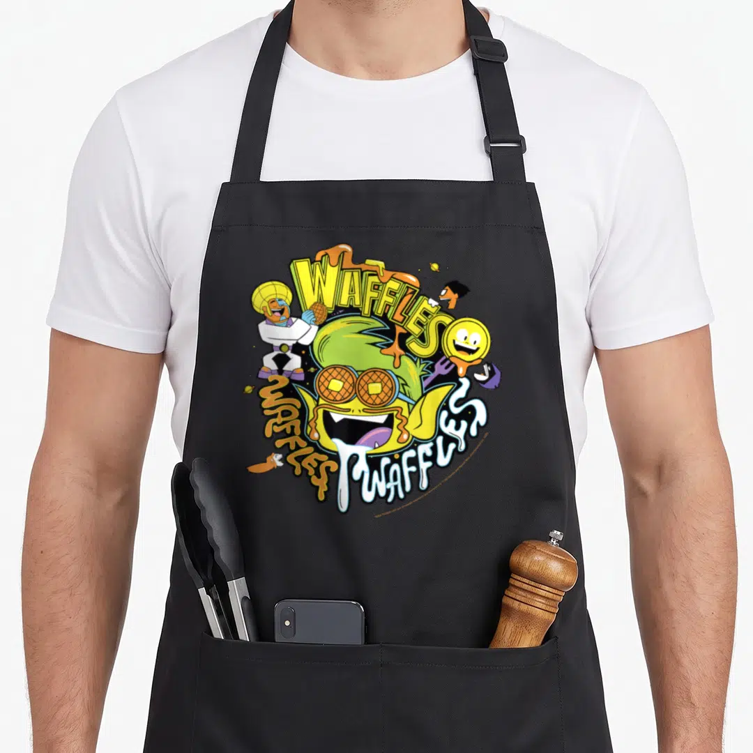 Beast waffle apron - Beast Boy with waffle eyes, Cyborg holding a waffle, and WAFFLES text in yellow and orange — shown on a black cotton canvas apron against a white background