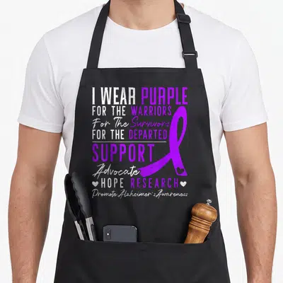 Awareness alzheimer's aprons - I WEAR PURPLE text with purple ribbon and two small hearts flanking hope research line — shown on a black cotton canvas apron against a white background
