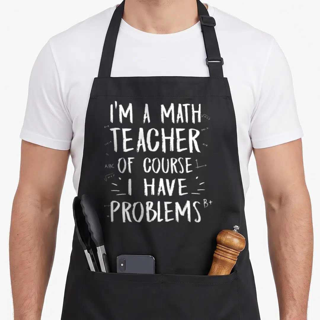 Funny course teacher apron - White stacked text I'm A Math Teacher Of Course I Have Problems with scattered equations — shown on a black cotton canvas apron against a white background