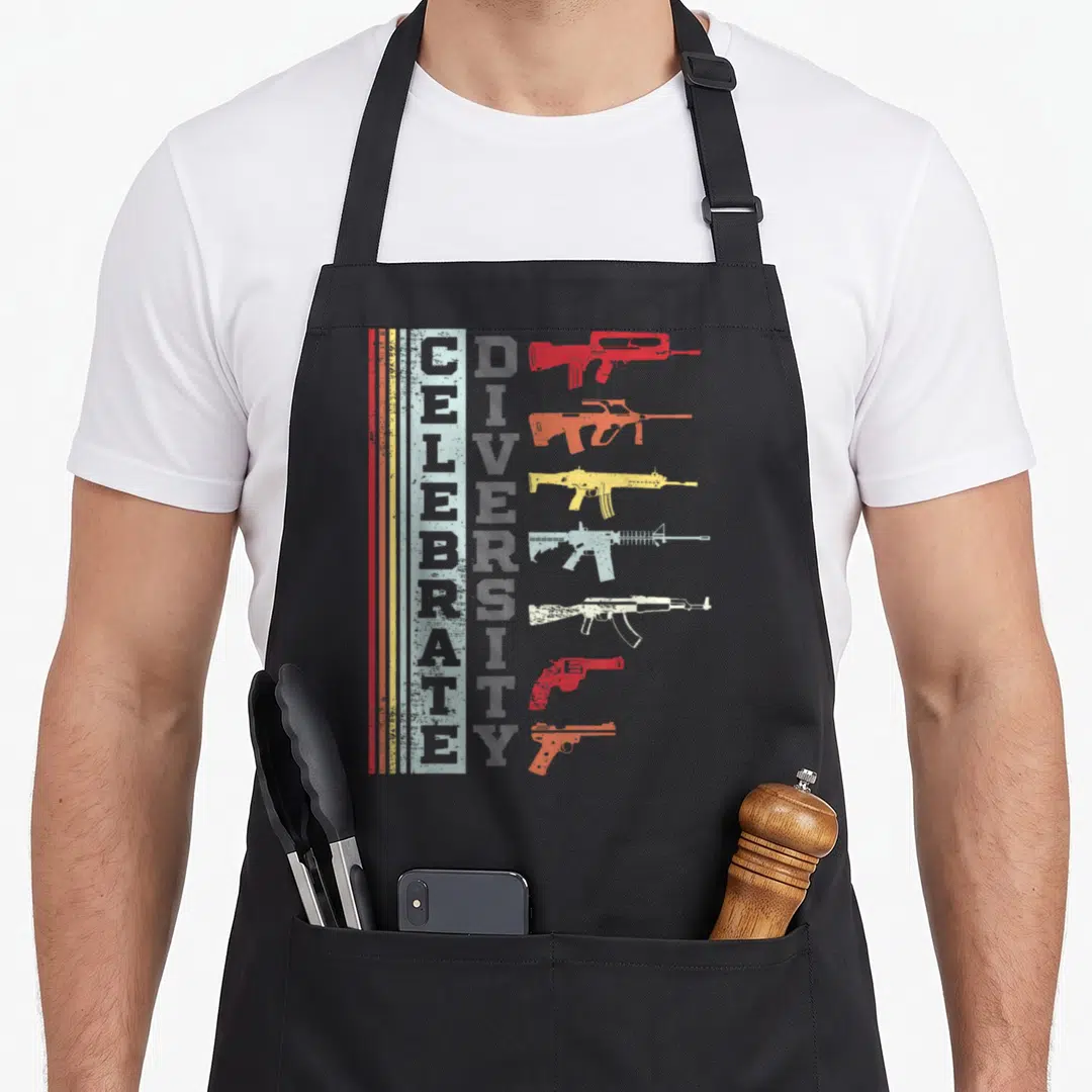 Different gun apron - Vertical CELEBRATE DIVERSITY text beside seven stacked colored gun silhouettes with distressed — shown on a black cotton canvas apron against a white background