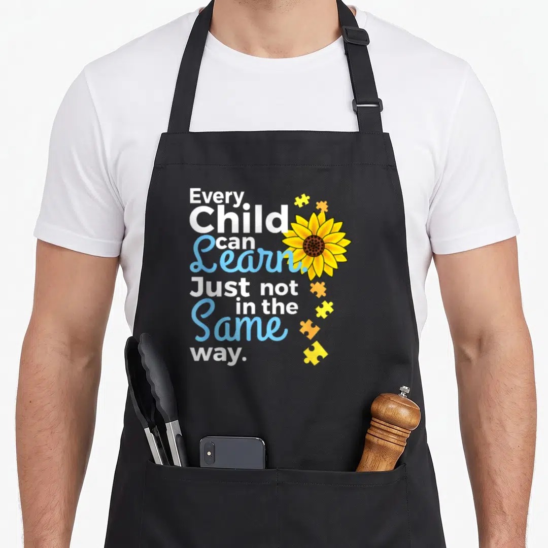 Special teacher art apron - Stacked text Every Child Can Learn with yellow sunflower and puzzle pieces — shown on a black cotton canvas apron against a white background