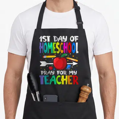 Homeschool pray teacher apron - Rainbow text 1st day homeschool pray for my teacher with red apple and stationery — shown on a black cotton canvas apron against a white background