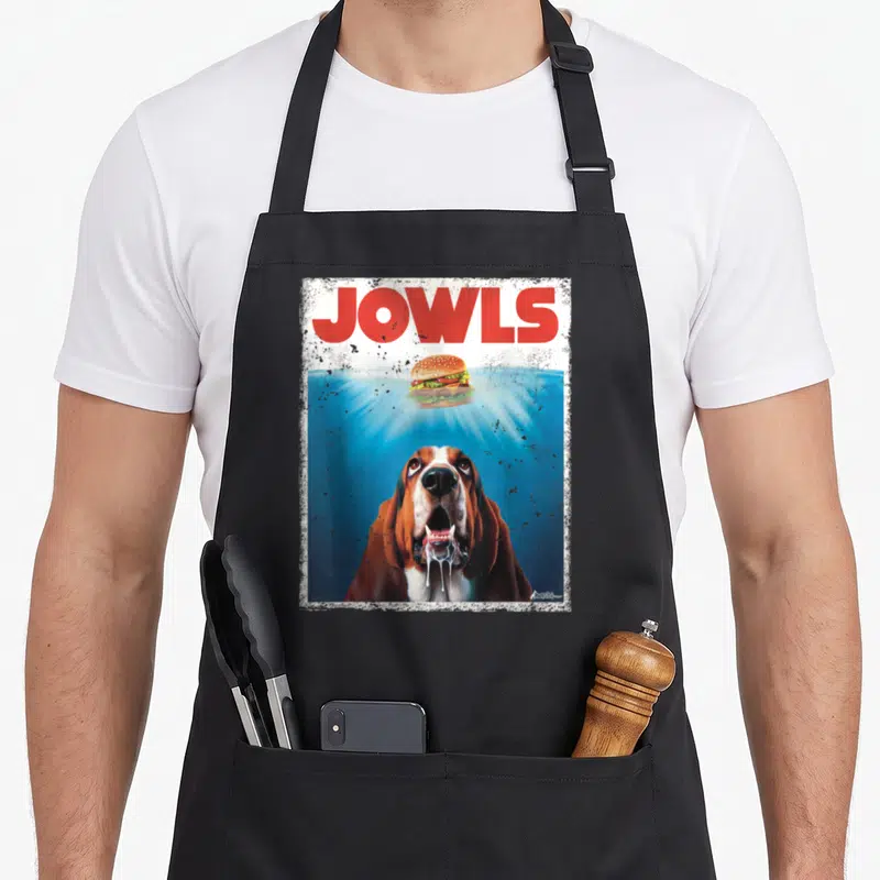 Bassett dog apron - Red Jowls text above bloodhound gazing at floating burger with light rays — shown on a black cotton canvas apron against a white background
