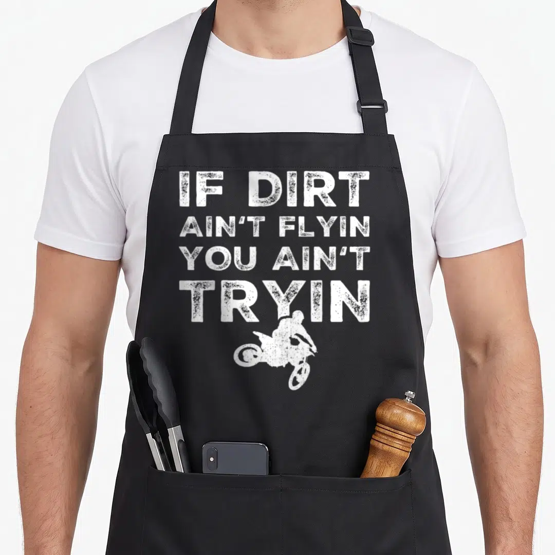 Dirt bike apron - White distressed text IF DIRT AIN'T FLYIN above motocross rider silhouette on black background — shown on a black cotton canvas apron against a white background