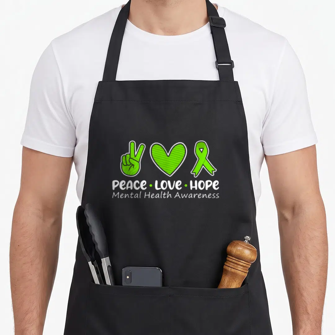 Peace ribbon apron - Green peace hand, heart, and ribbon with white Peace Love Hope text — shown on a black cotton canvas apron against a white background