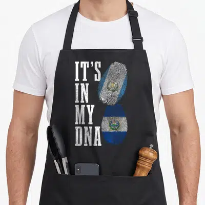Salvador guatemalan aprons - IT'S IN MY DNA text next to stacked fingerprint flags in Guatemalan and Salvadorian colors — shown on a black cotton canvas apron against a white background