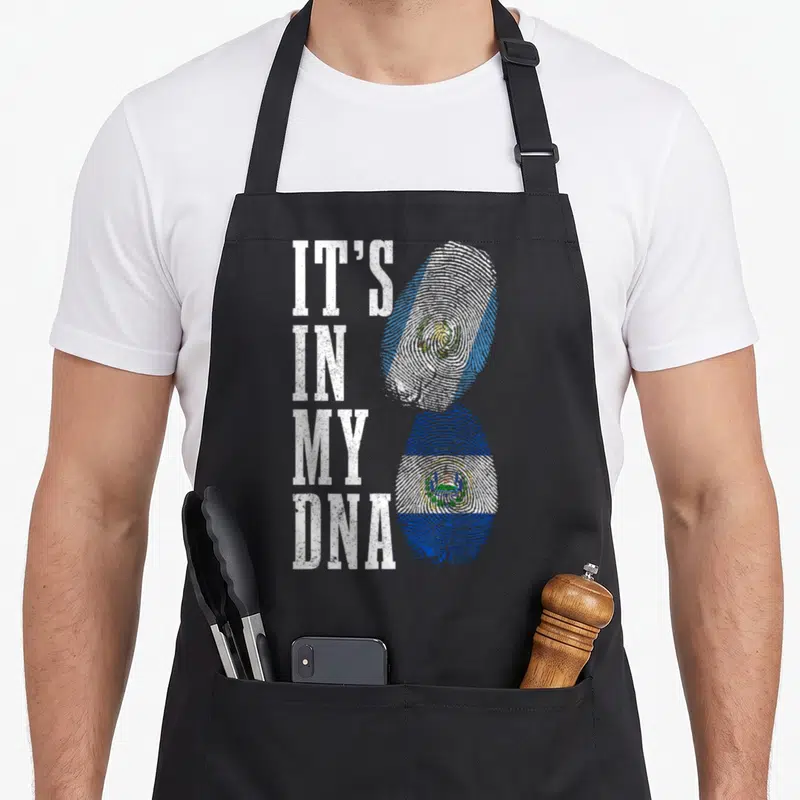 Salvador guatemalan aprons - IT'S IN MY DNA text next to stacked fingerprint flags in Guatemalan and Salvadorian colors — shown on a black cotton canvas apron against a white background
