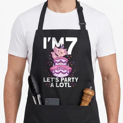 Bday axolotl birthday apron - Pink axolotl on two-tier cake with I'M 7 and party a lotl text — shown on a black cotton canvas apron against a white background