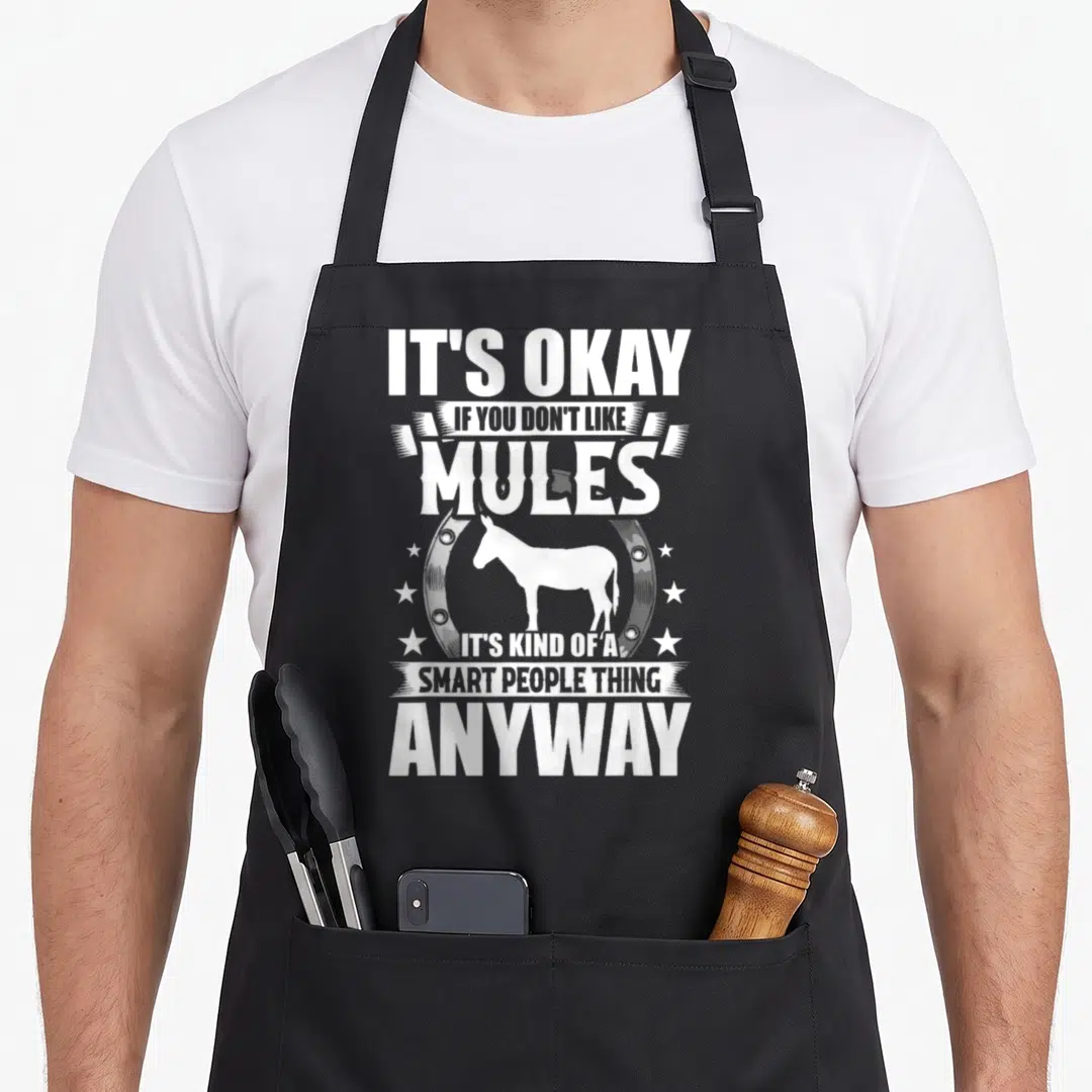 Okay mule apron - White mule silhouette inside horseshoe with stacked sarcastic text — shown on a black cotton canvas apron against a white background