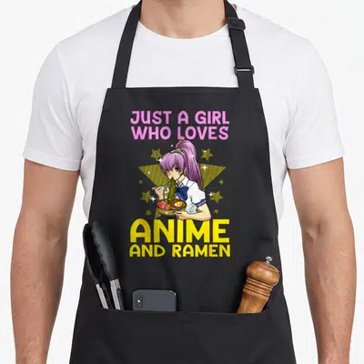 Cool ramen anime apron - Girl with purple ponytail eating ramen bowl under pink and yellow text with stars — shown on a black cotton canvas apron against a white background