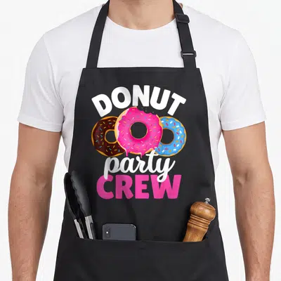Crew donut apron - Three overlapping pink blue and brown doughnuts with stacked DONUT party CREW text — shown on a black cotton canvas apron against a white background