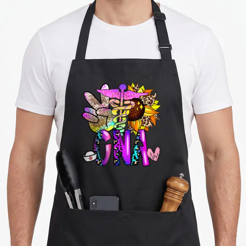 Peace nurse apron - CNA text with peace sign, caduceus, sunflower, nurse hat, heart, leopard print in purple pink — shown on a black cotton canvas apron against a white background