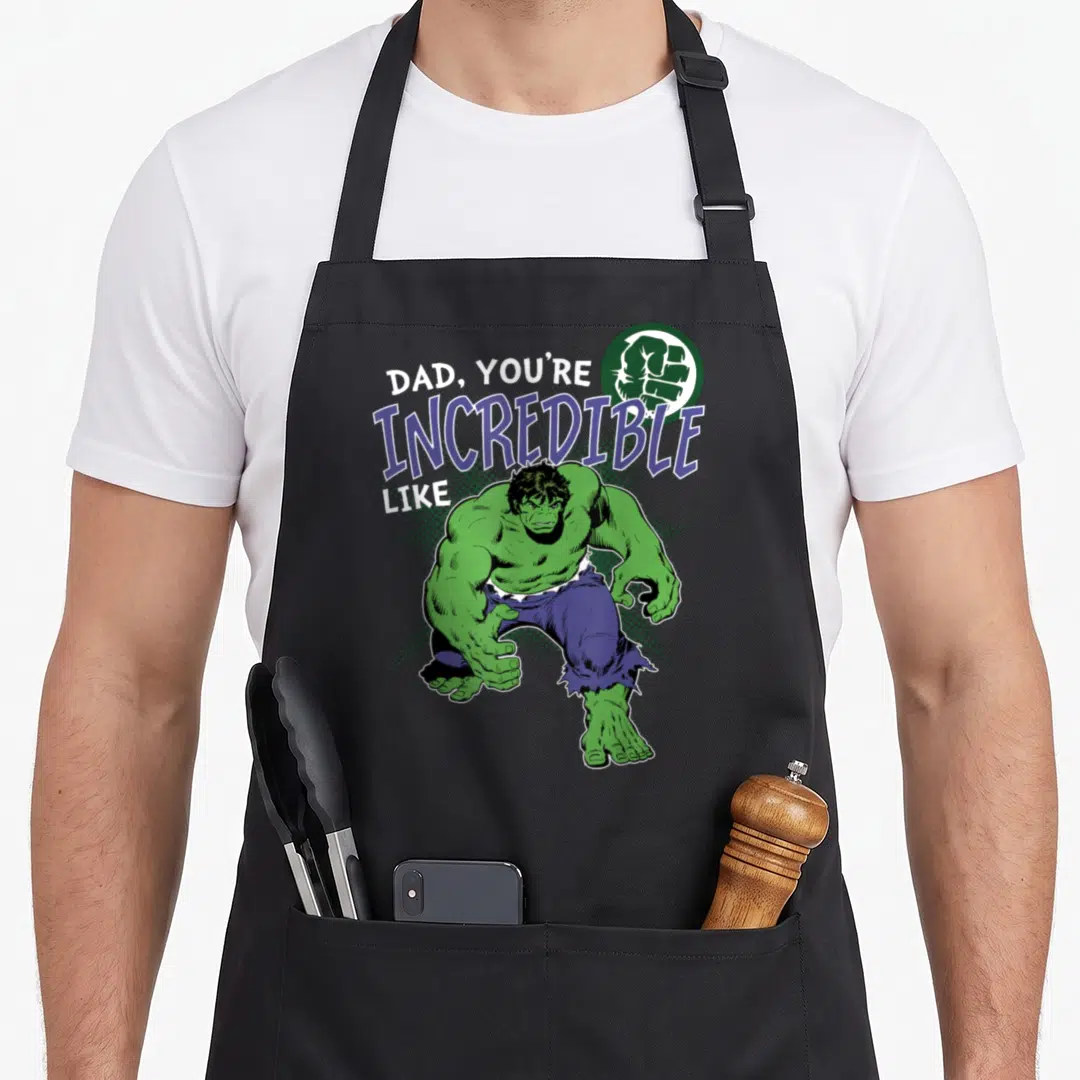 Retro incredible father day apron - Green cartoon character crouching below white and purple text reading DAD YOU'RE — shown on a black cotton canvas apron against a white background