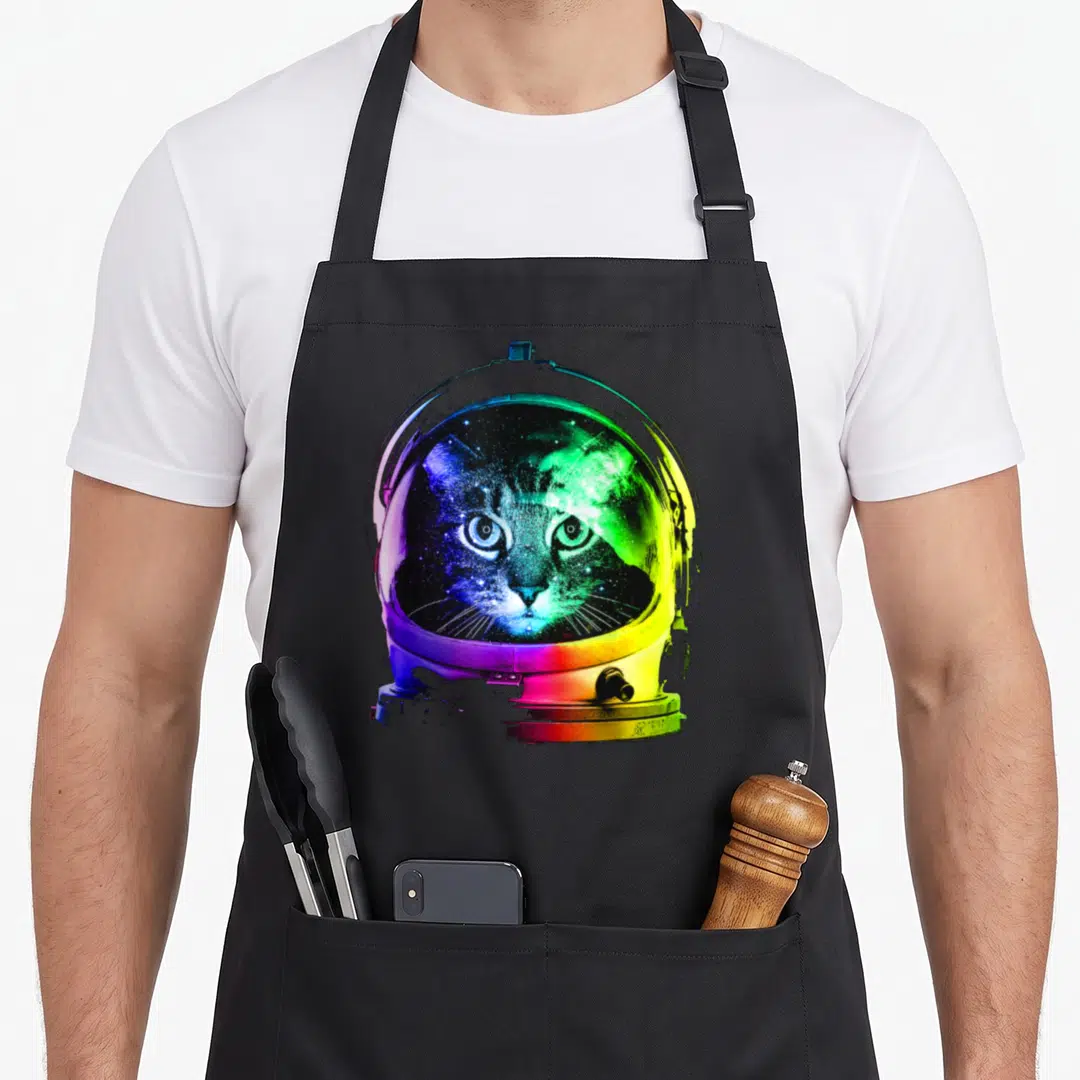 Funny astronaut space cat apron - Realistic cat face inside rainbow colored astronaut helmet visor — shown on a black cotton canvas apron against a white background