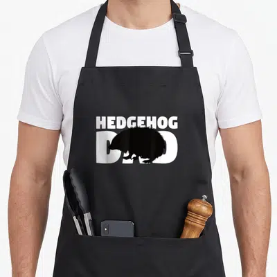 Hedgehog father animal apron - White HEDGEHOG DAD text with black hedgehog silhouette overlapping the bottom line — shown on a black cotton canvas apron against a white background