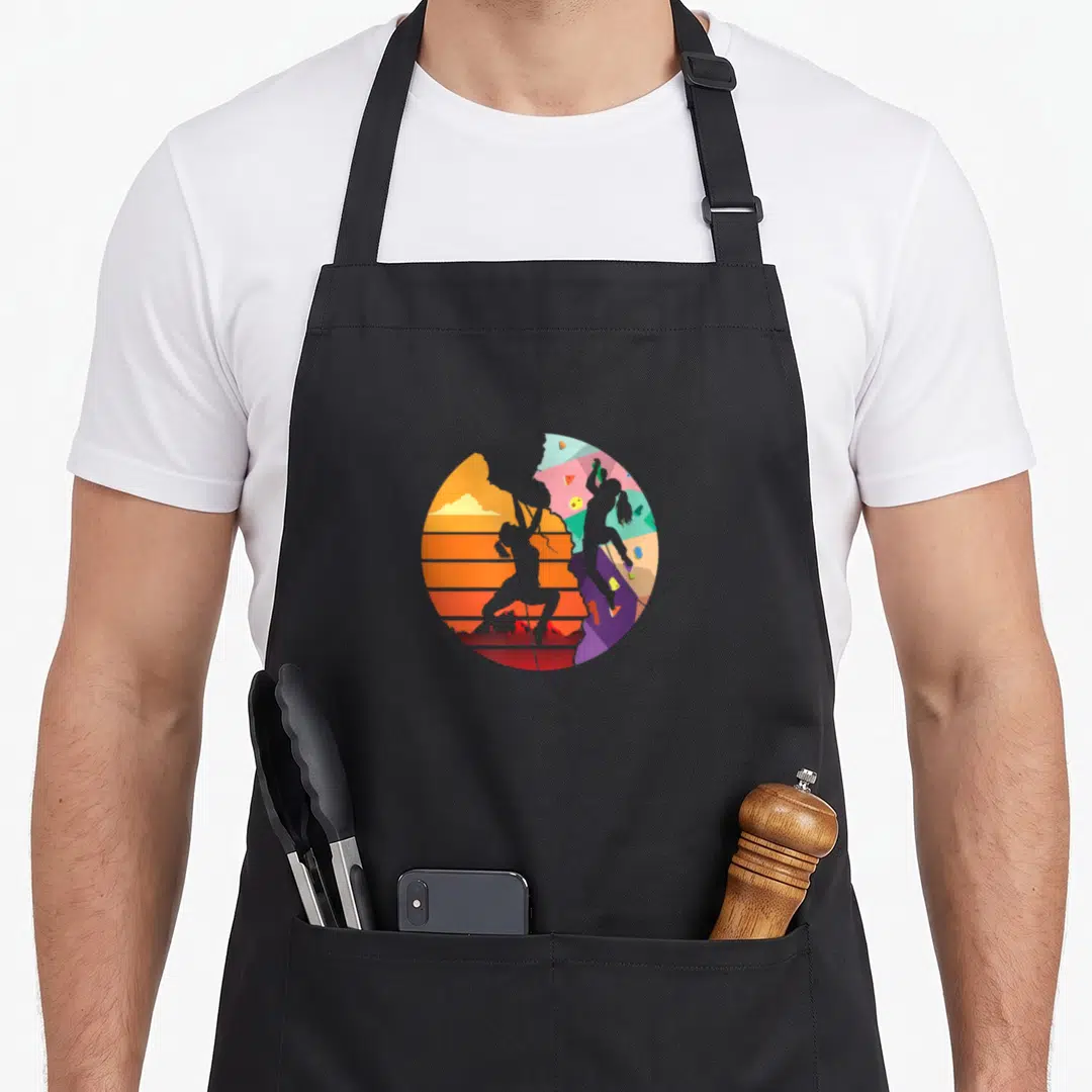 Sport bouldering apron - Circular split design of grey rock climber silhouettes against orange sunset and colorful — shown on a black cotton canvas apron against a white background