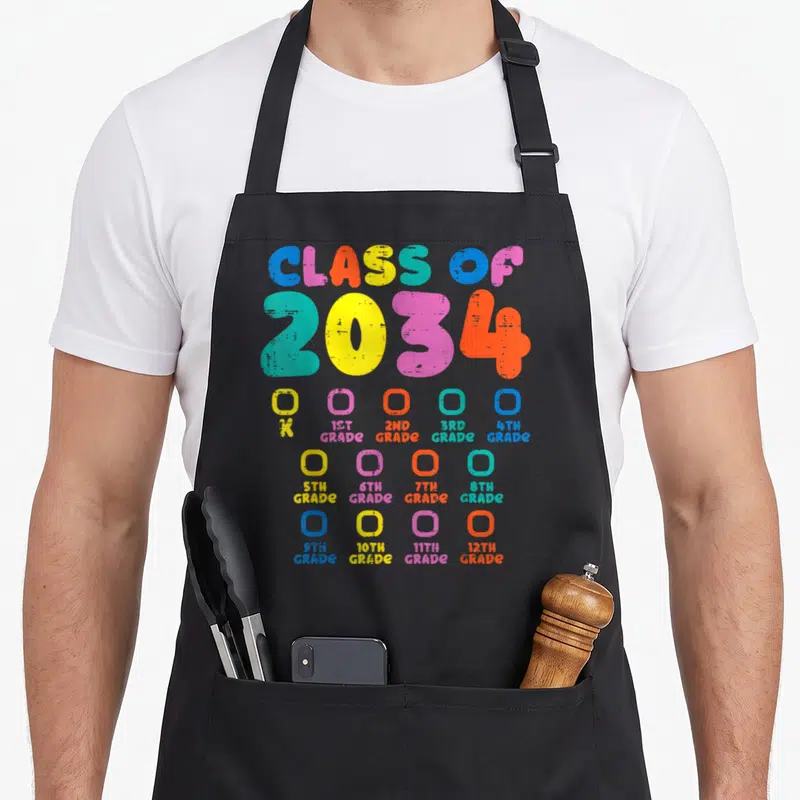Class colorful aprons - Class of 2034 grade checklist K to 12th in blue pink yellow orange cyan typography — shown on a black cotton canvas apron against a white background