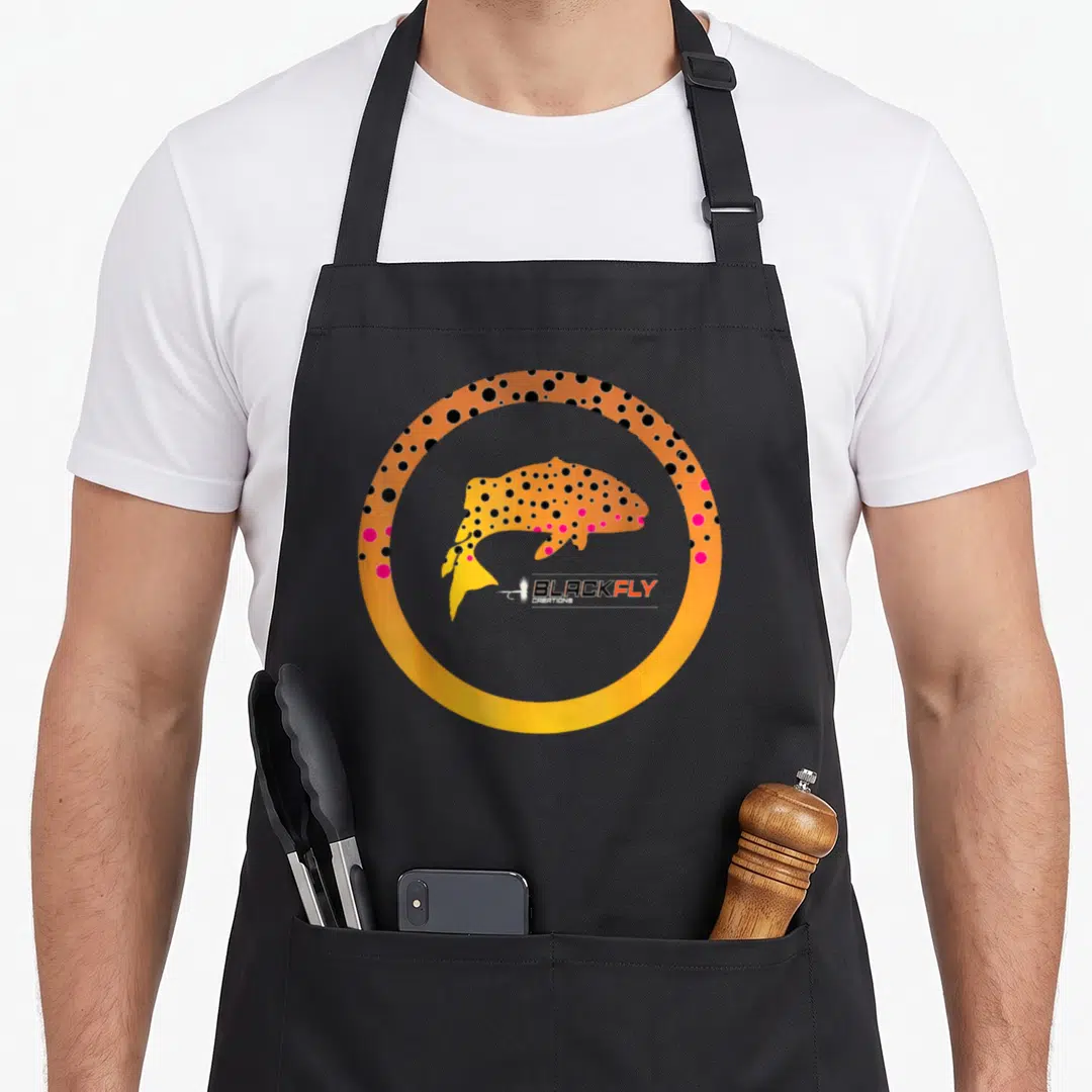 Skin fishing aprons - Orange spotted fish inside a thick circular border with pink and black dots — shown on a black cotton canvas apron against a white background