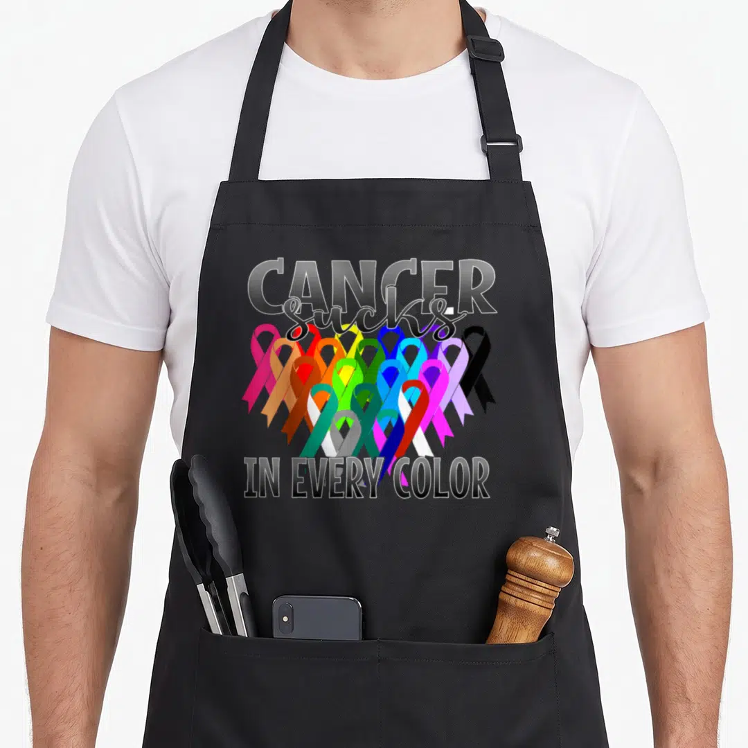 Suck cancer girl apron - Cancer Sucks in Every Color text with multicolored awareness ribbons — shown on a black cotton canvas apron against a white background
