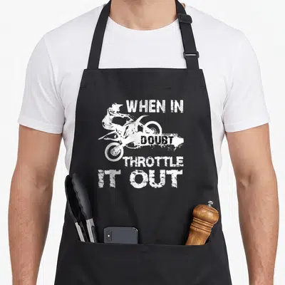 Motocross biker bike apron - White silhouette of a motocross rider surrounded by the text WHEN IN DOUBT THROTTLE IT OUT — shown on a black cotton canvas apron against a white background