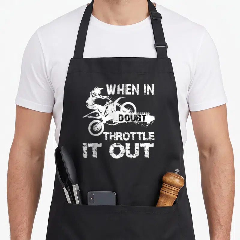 Motocross biker bike apron - White silhouette of a motocross rider surrounded by the text WHEN IN DOUBT THROTTLE IT OUT — shown on a black cotton canvas apron against a white background