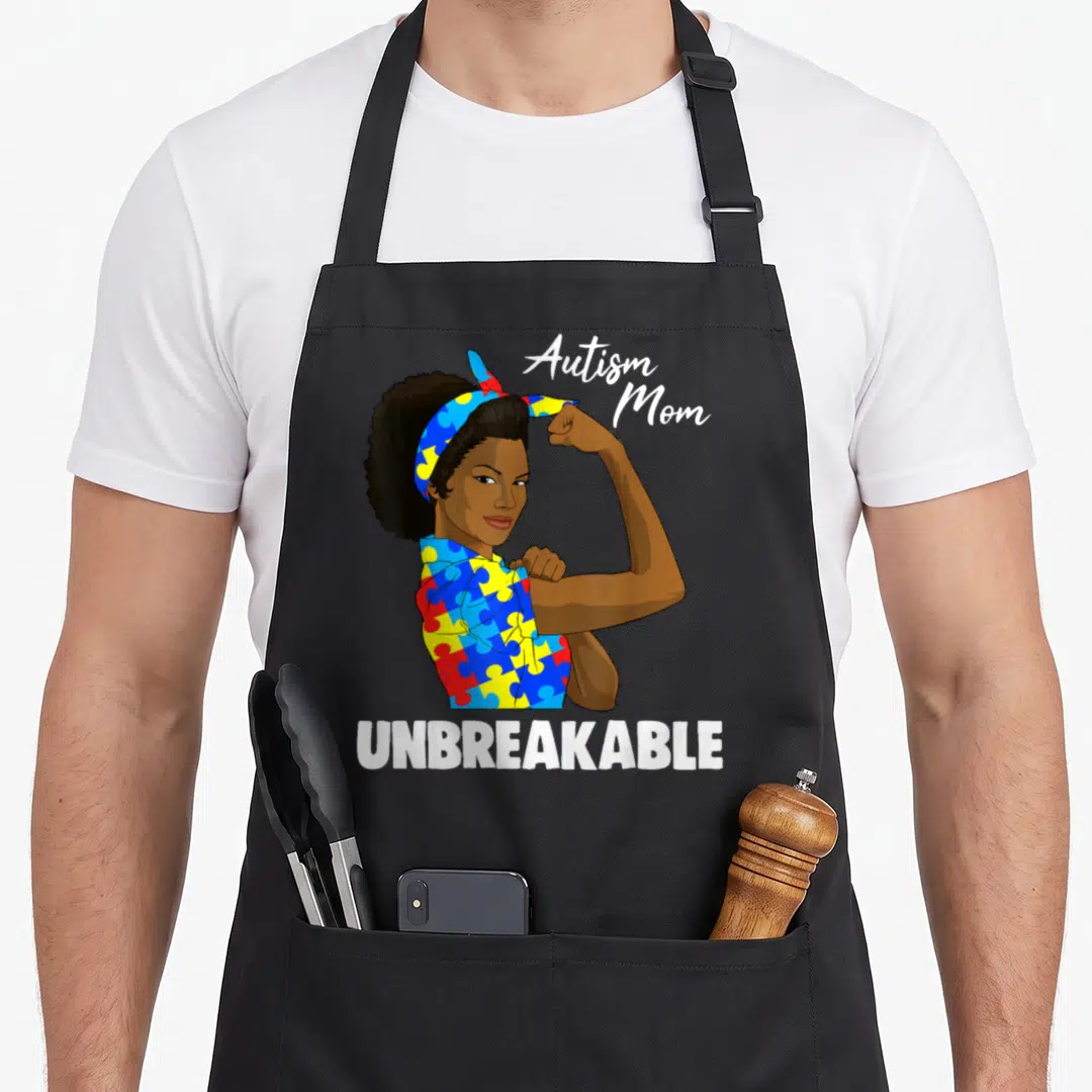 Awareness special needs mom apron - Cartoon woman flexing in blue red yellow white puzzle pieces with Autism Mom — shown on a black cotton canvas apron against a white background