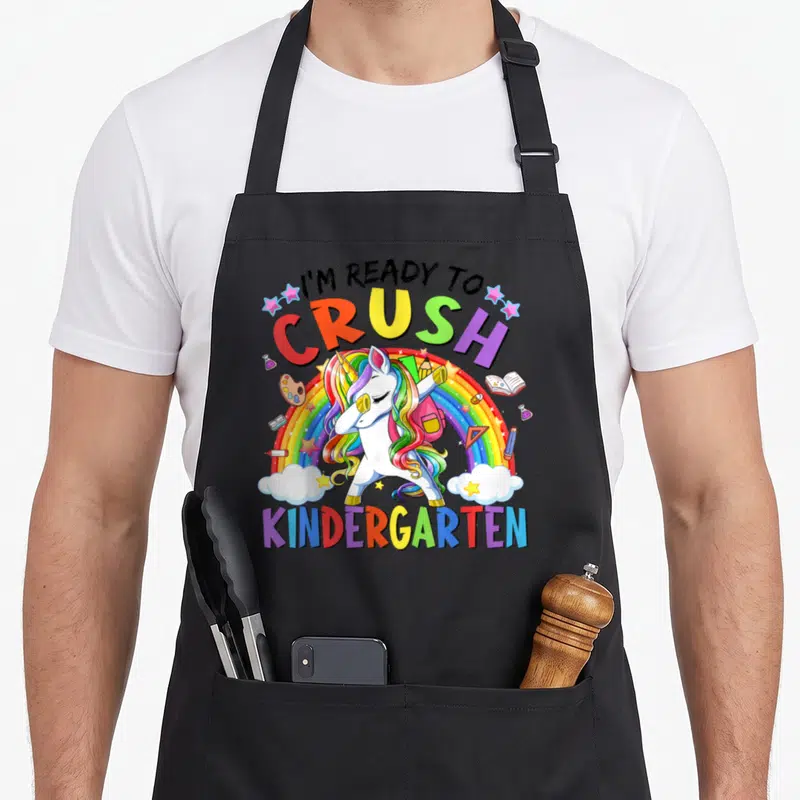 Crush kindergarten teacher apron - Dabbing unicorn over rainbow with school supplies and text I'm ready to crush — shown on a black cotton canvas apron against a white background