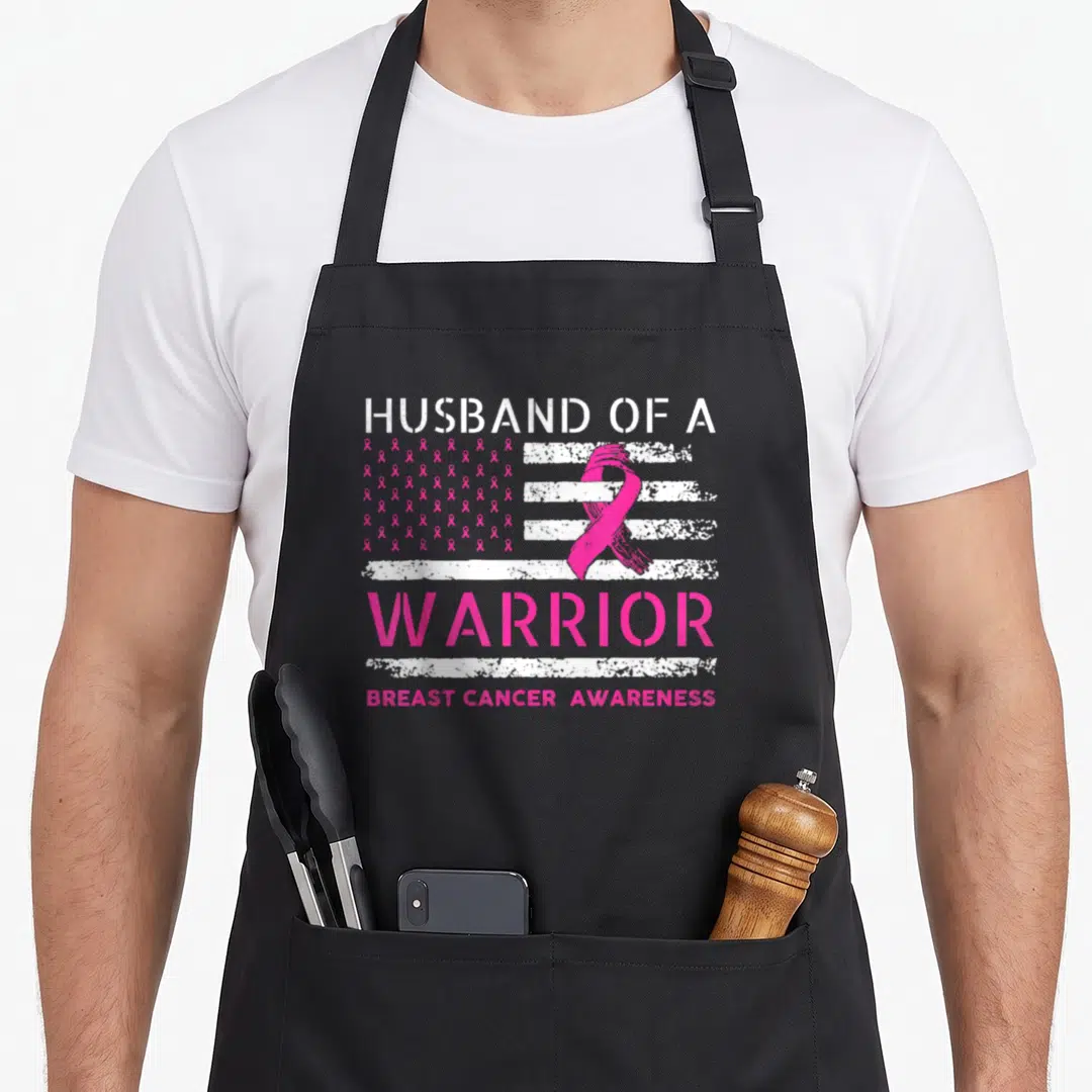 Support squad breast cancer awareness aprons - Distressed pink ribbon flag with Husband of a Warrior text and breast — shown on a black cotton canvas apron against a white background