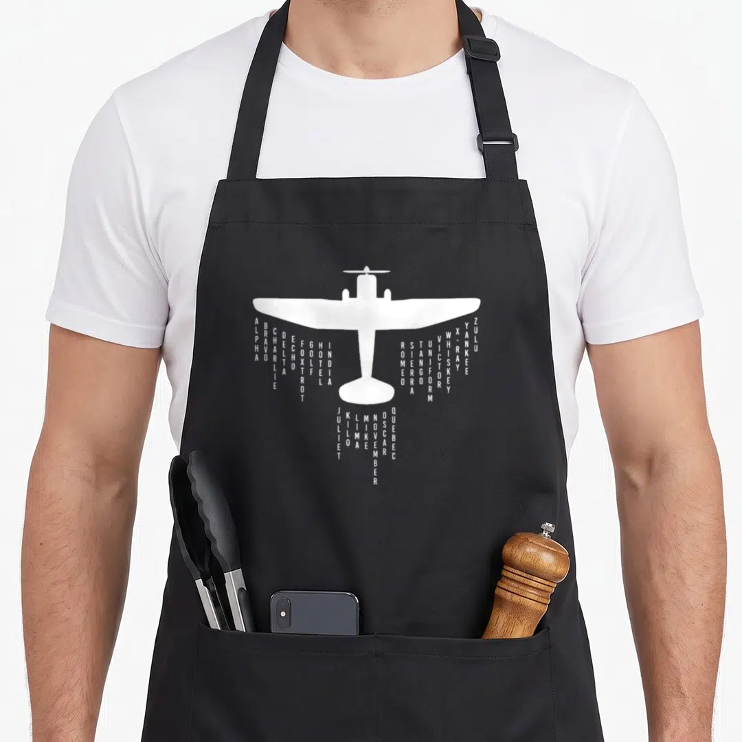 Alphabet pilot airplane apron - White airplane silhouette with vertical phonetic alphabet words hanging from wings — shown on a black cotton canvas apron against a white background