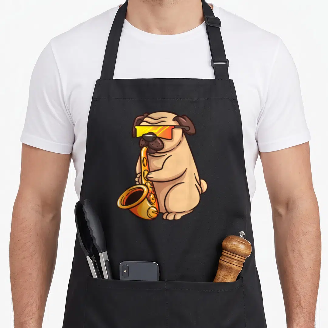 Saxophone dog apron - Cartoon tan pug wearing gold sunglasses and playing an orange saxophone — shown on a black cotton canvas apron against a white background