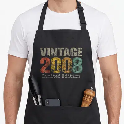 Cute 18th age birthday apron - Vintage 2008 Limited Edition distressed text in beige red yellow orange green — shown on a black cotton canvas apron against a white background