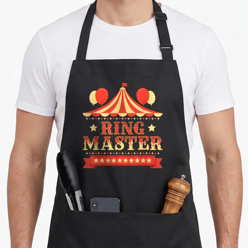 Circus costume birthday apron - Red and yellow circus tent with RING MASTER text and star ribbon — shown on a black cotton canvas apron against a white background