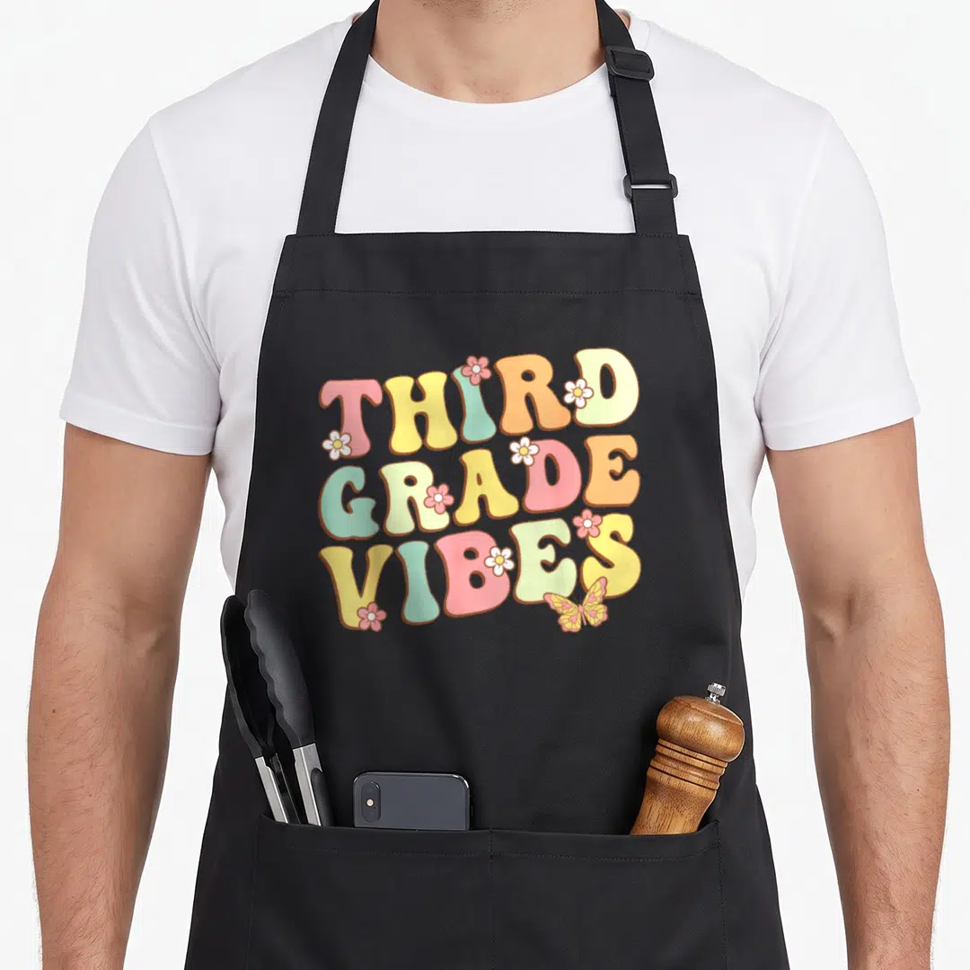 Grade hello teacher apron - Stacked bubbly text THIRD GRADE VIBES with flowers and butterfly in pink yellow blue orange — shown on a black cotton canvas apron against a white background