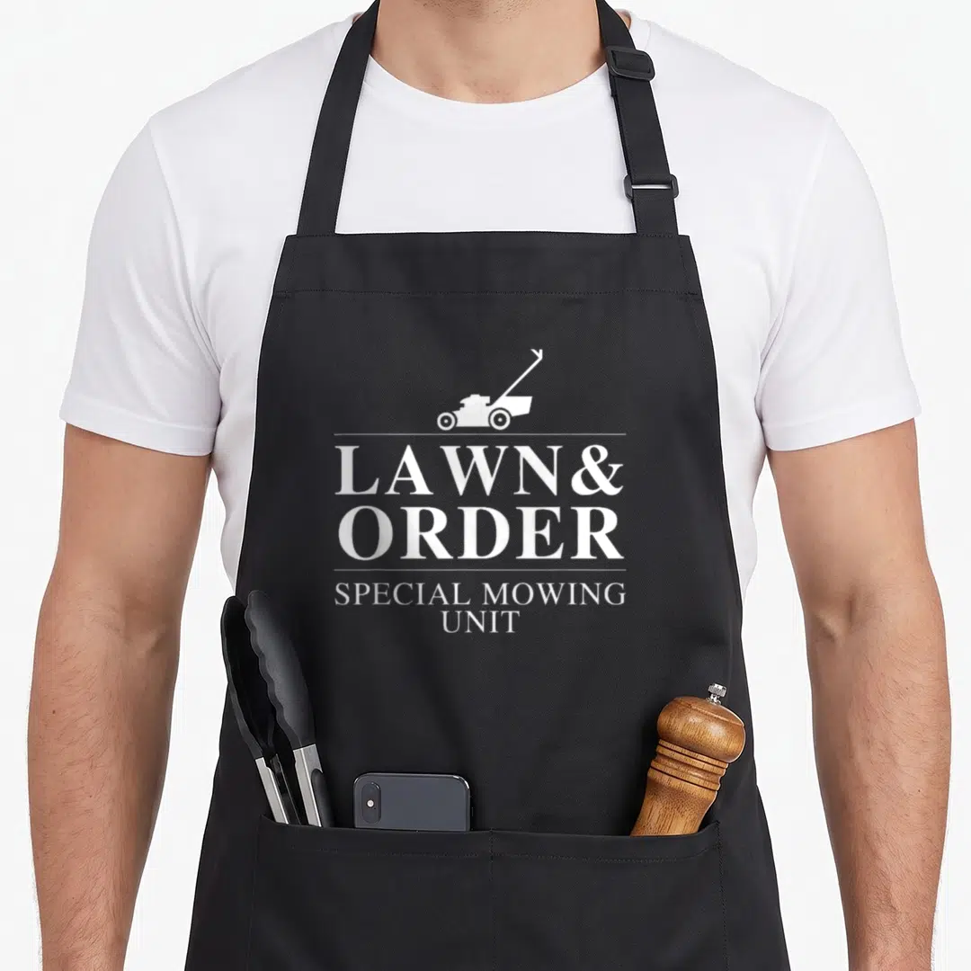 Lawn joke apron - White LAWN & ORDER text with mower silhouette and SPECIAL MOWING UNIT below — shown on a black cotton canvas apron against a white background