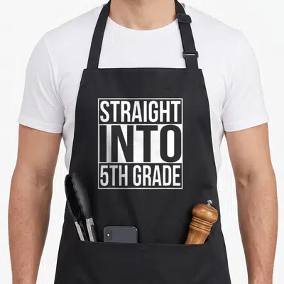 Straight fifth grade apron - White text reading STRAIGHT INTO 5TH GRADE in stacked layout inside white rectangle — shown on a black cotton canvas apron against a white background