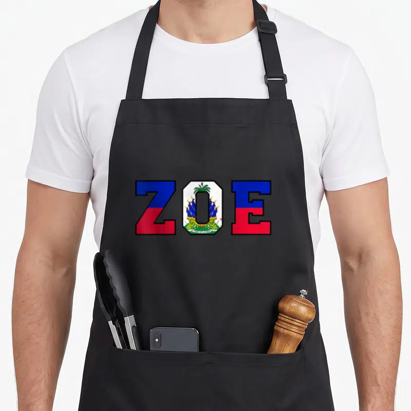 Zoe pride apron - ZOE text with Haitian flag blue red white fill and coat of arms in center letter — shown on a black cotton canvas apron against a white background