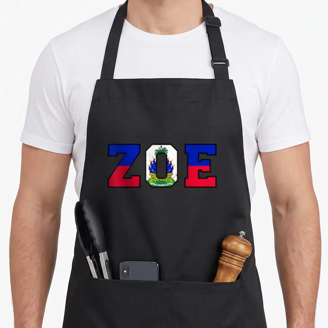 Zoe pride apron - ZOE text with Haitian flag blue red white fill and coat of arms in center letter — shown on a black cotton canvas apron against a white background