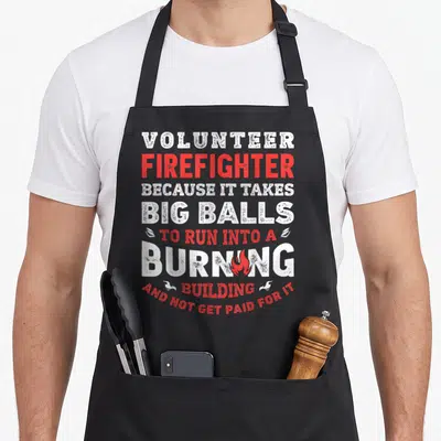 Volunteer firefighter apron - Stacked white and red distressed text reading Volunteer Firefighter Because It Takes Big — shown on a black cotton canvas apron against a white background